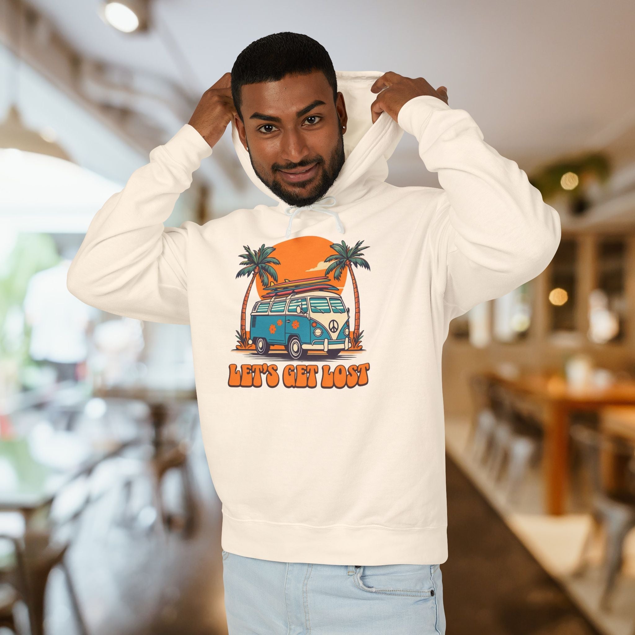 Man wearing a white hoodie with a graphic design of a van and palm trees, text 'Let's Get Lost', in a casual setting.