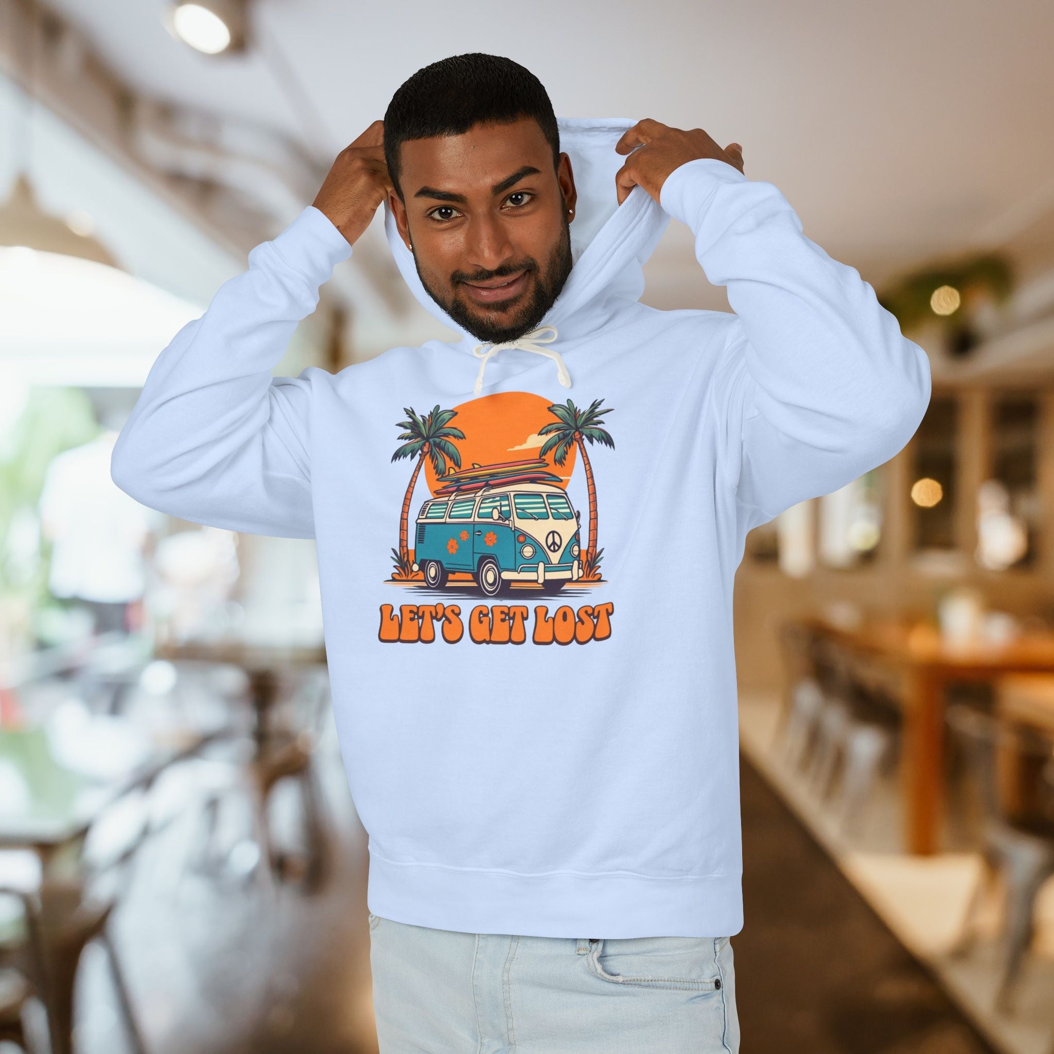 Man wearing a white hoodie with a graphic design of a van and palm trees, text 'Let's Get Lost', in an indoor setting.