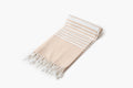 Beige and white striped towel with fringes on a light gray background