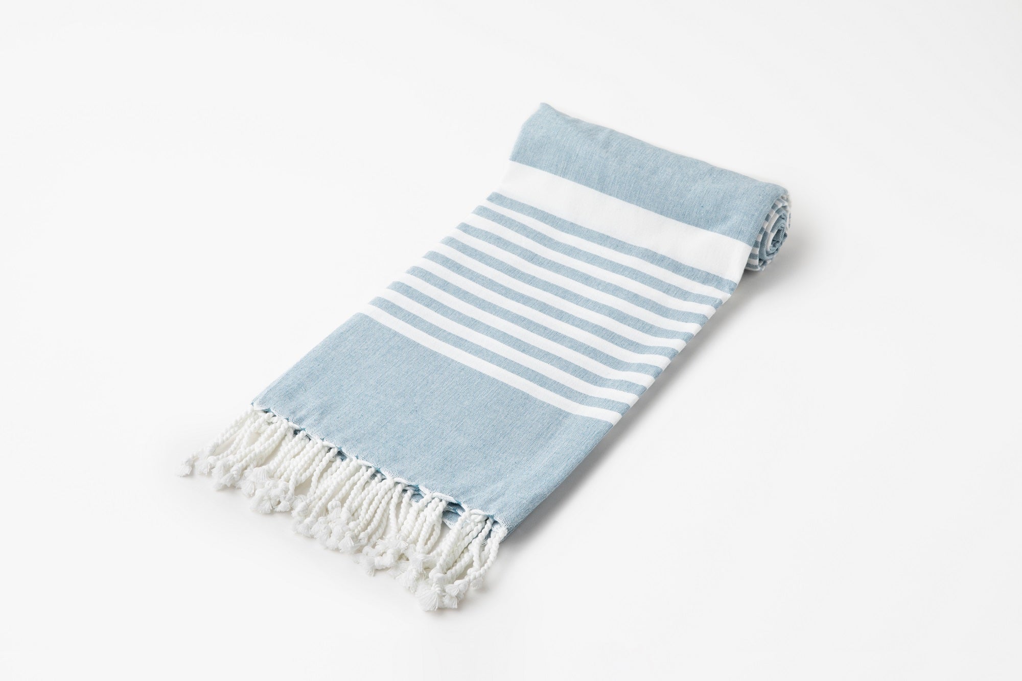 Rolled-up blue and white striped towel with tassels on a light gray background