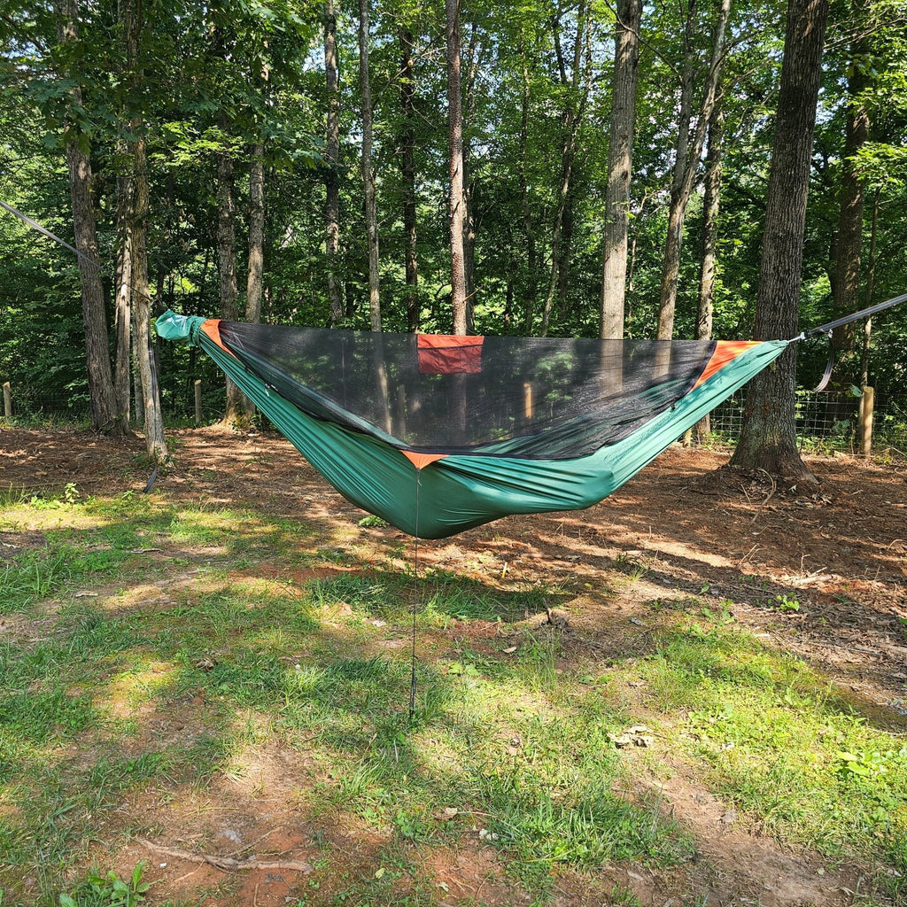 Green hammock with a canopy hanging between trees in a forest