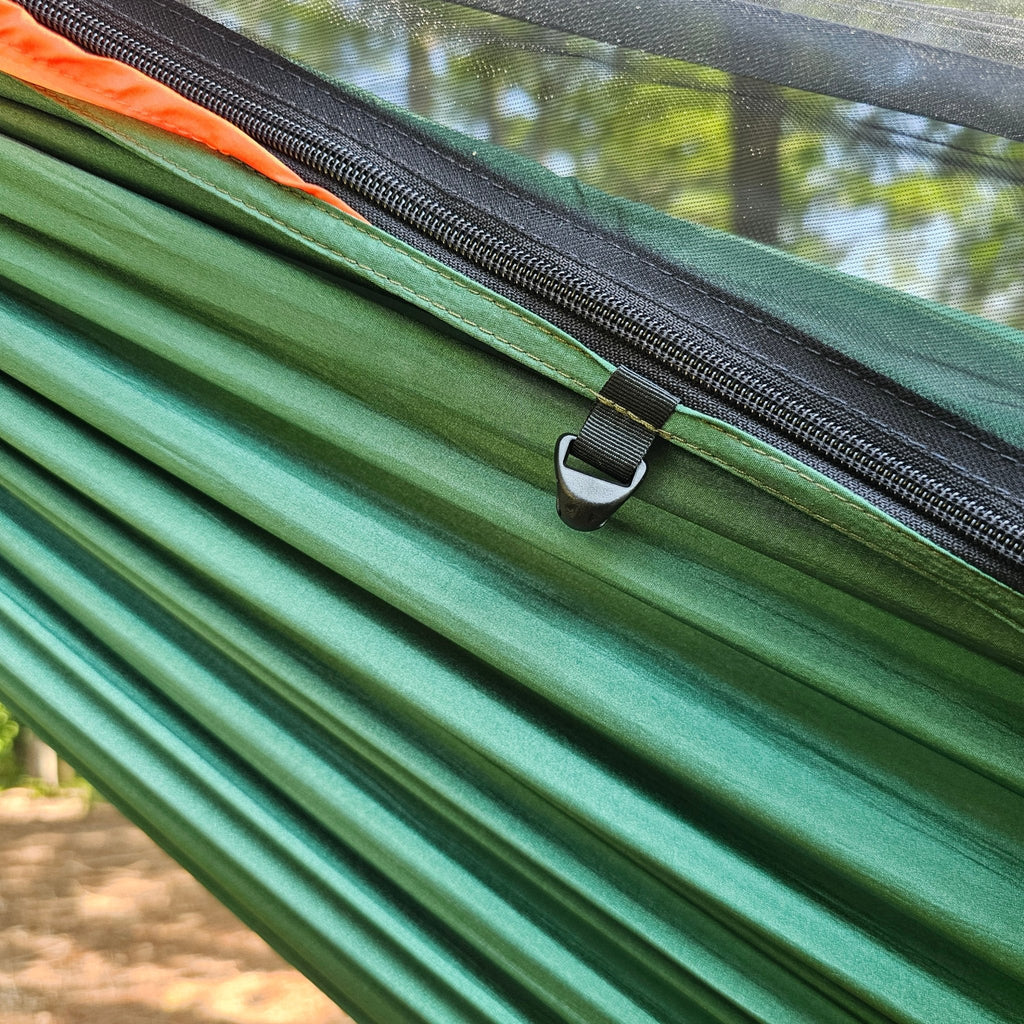 Green hammock with a black zipper and orange strap, set against a natural background.