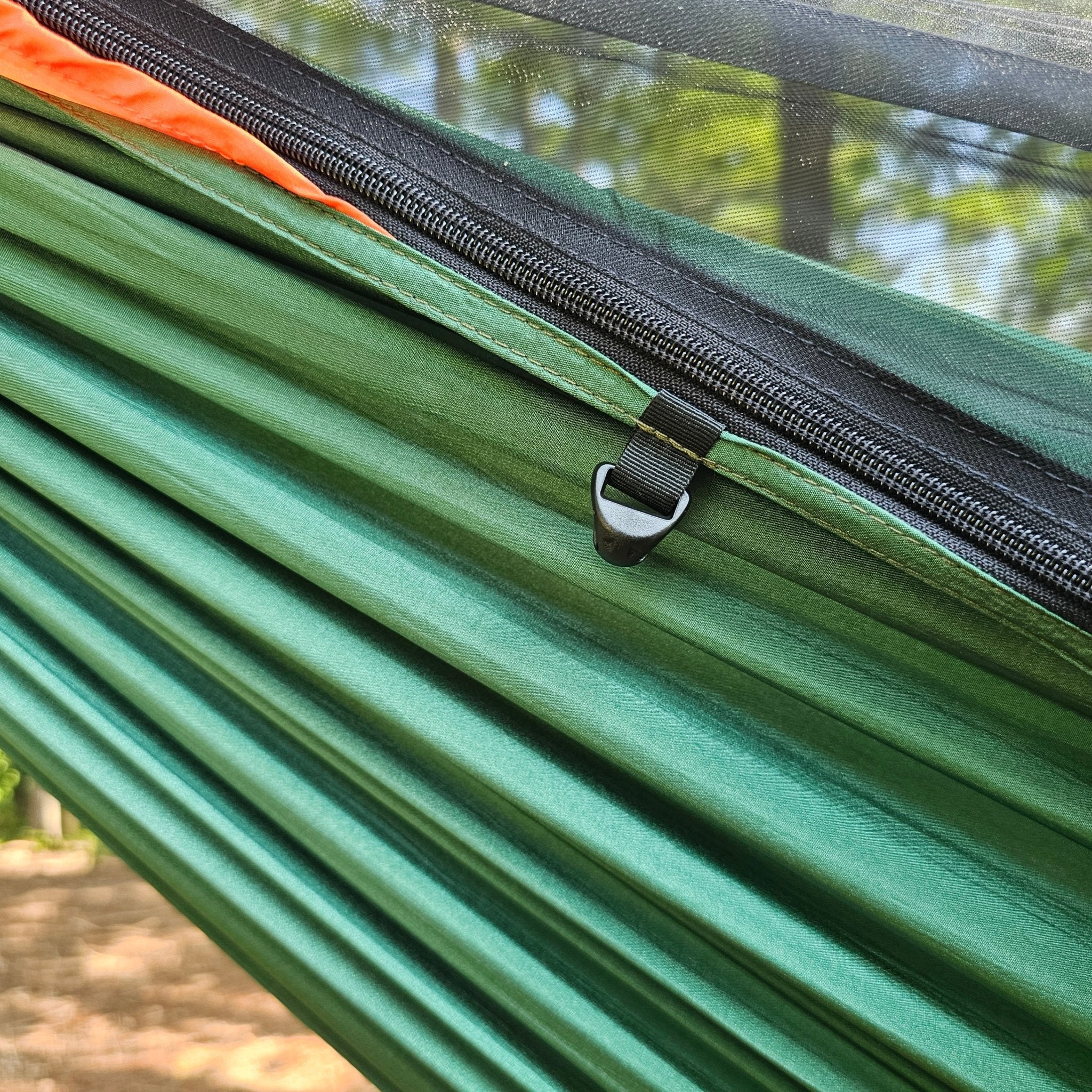 Green hammock with a black zipper and orange strap, set against a natural background.