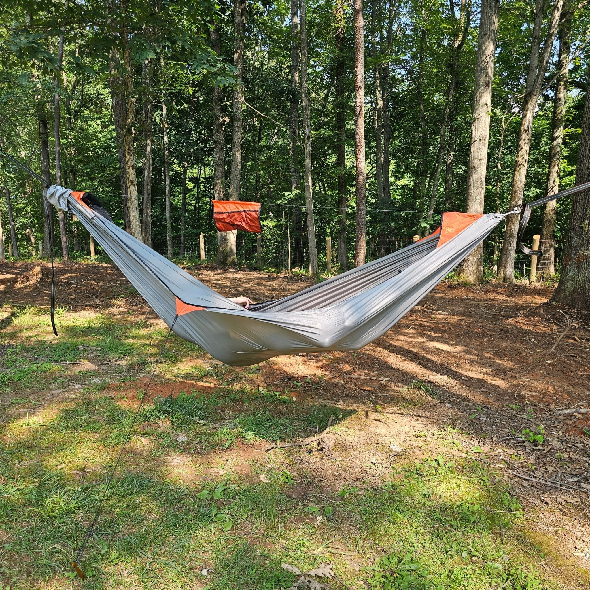 Gray hammock with orange accents hanging between trees in a forest setting