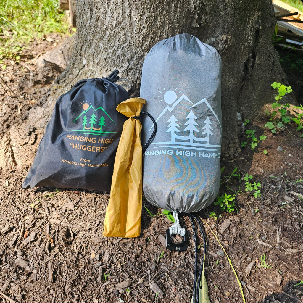 Two hammock bags with 'Hanging High Hammocks' branding against a tree trunk.
