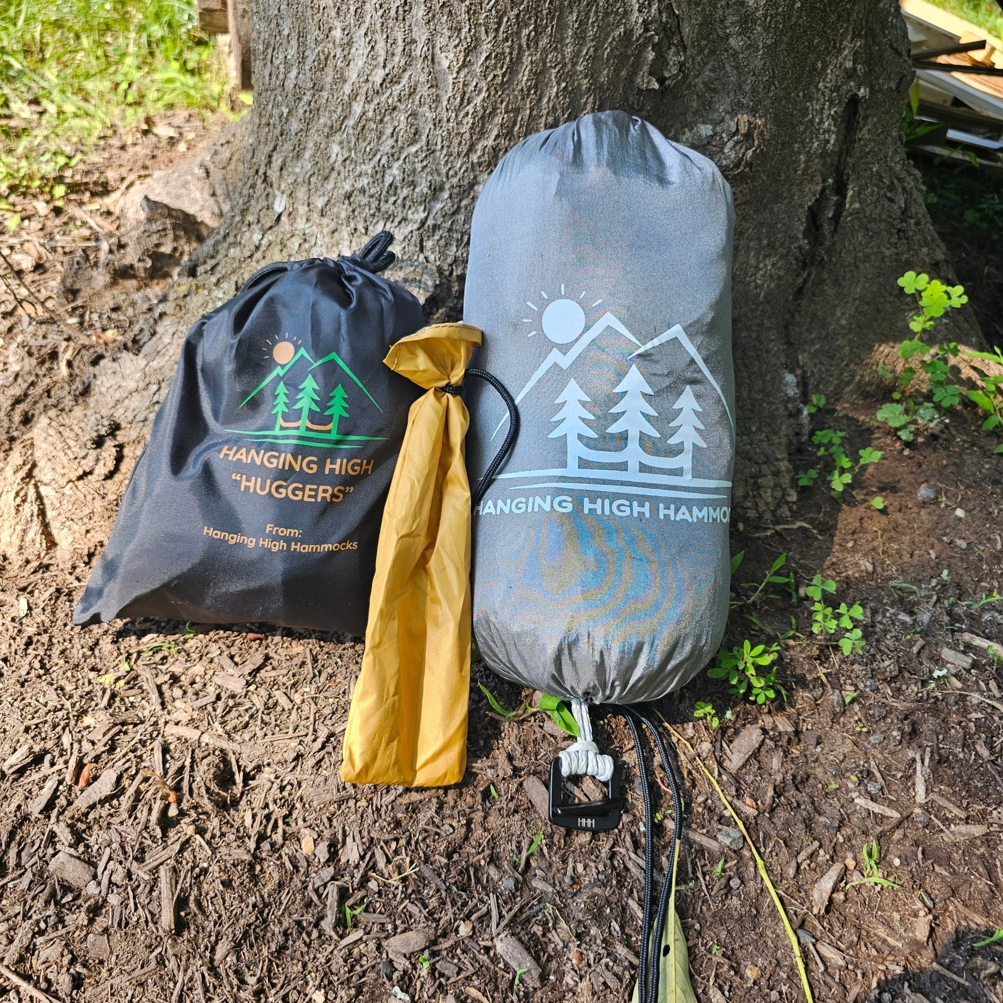 Two hammock bags with 'Hanging High Hammocks' branding against a tree trunk.